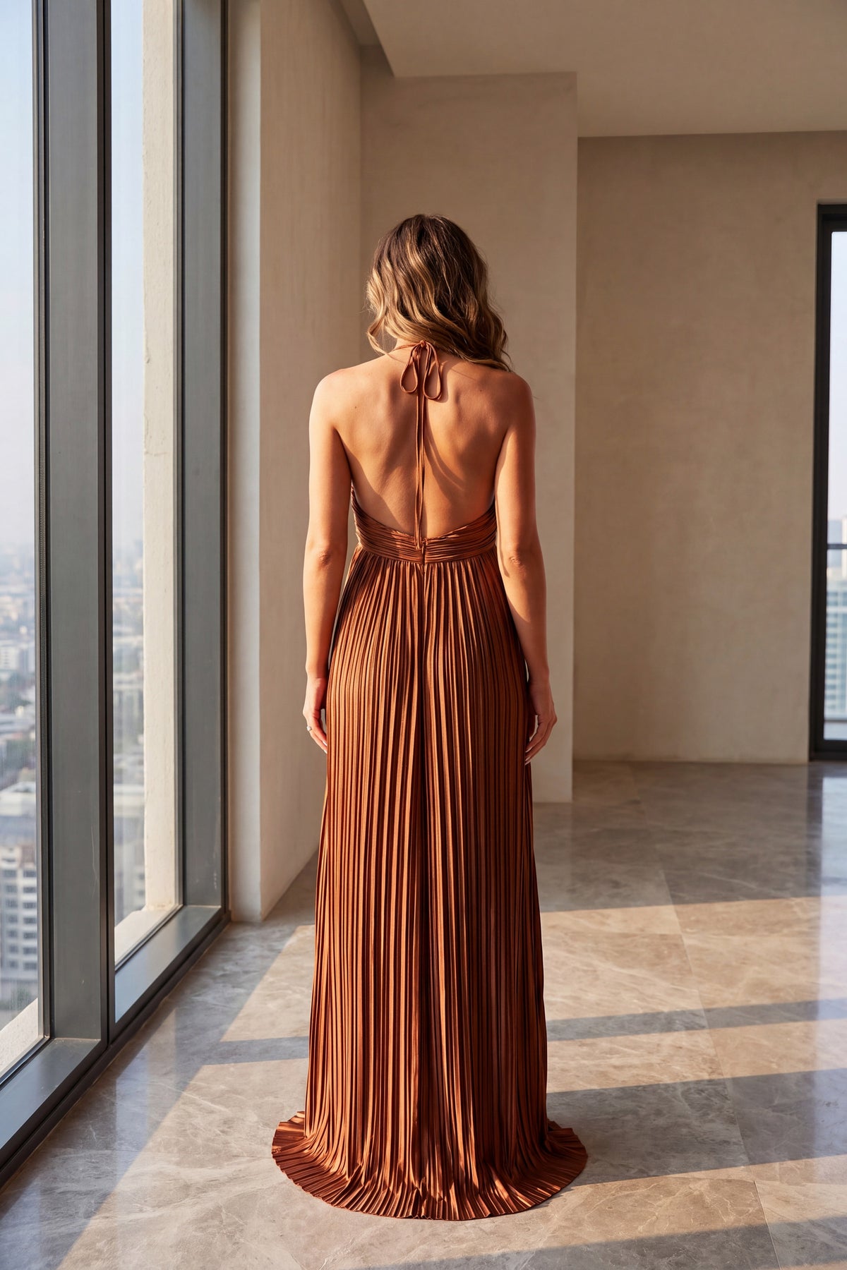 Liora rust satin plisse halter maxi dress, back view beside a tall window