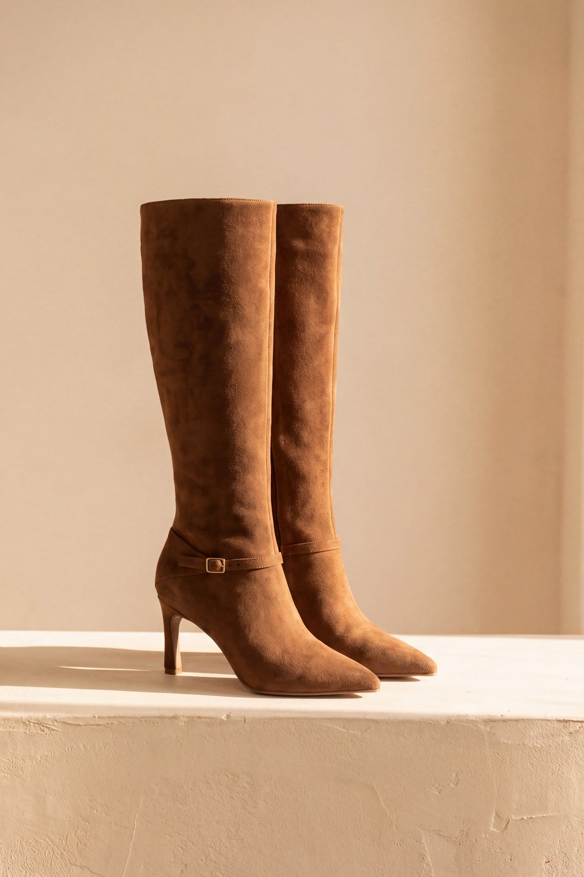 Vesper knee high boots pair standing on a warm plaster ledge in afternoon sun