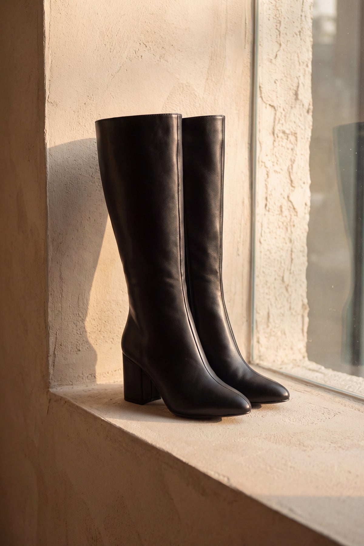 Nadia black extra wide calf knee high boot, pair standing on a warm plaster ledge