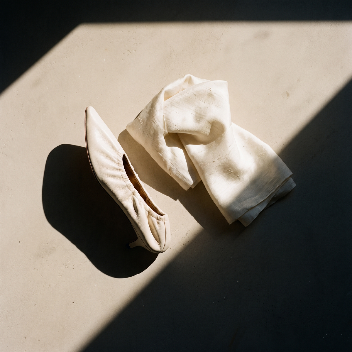 Ivory silk and a cream leather shoe on warm plaster in afternoon sun