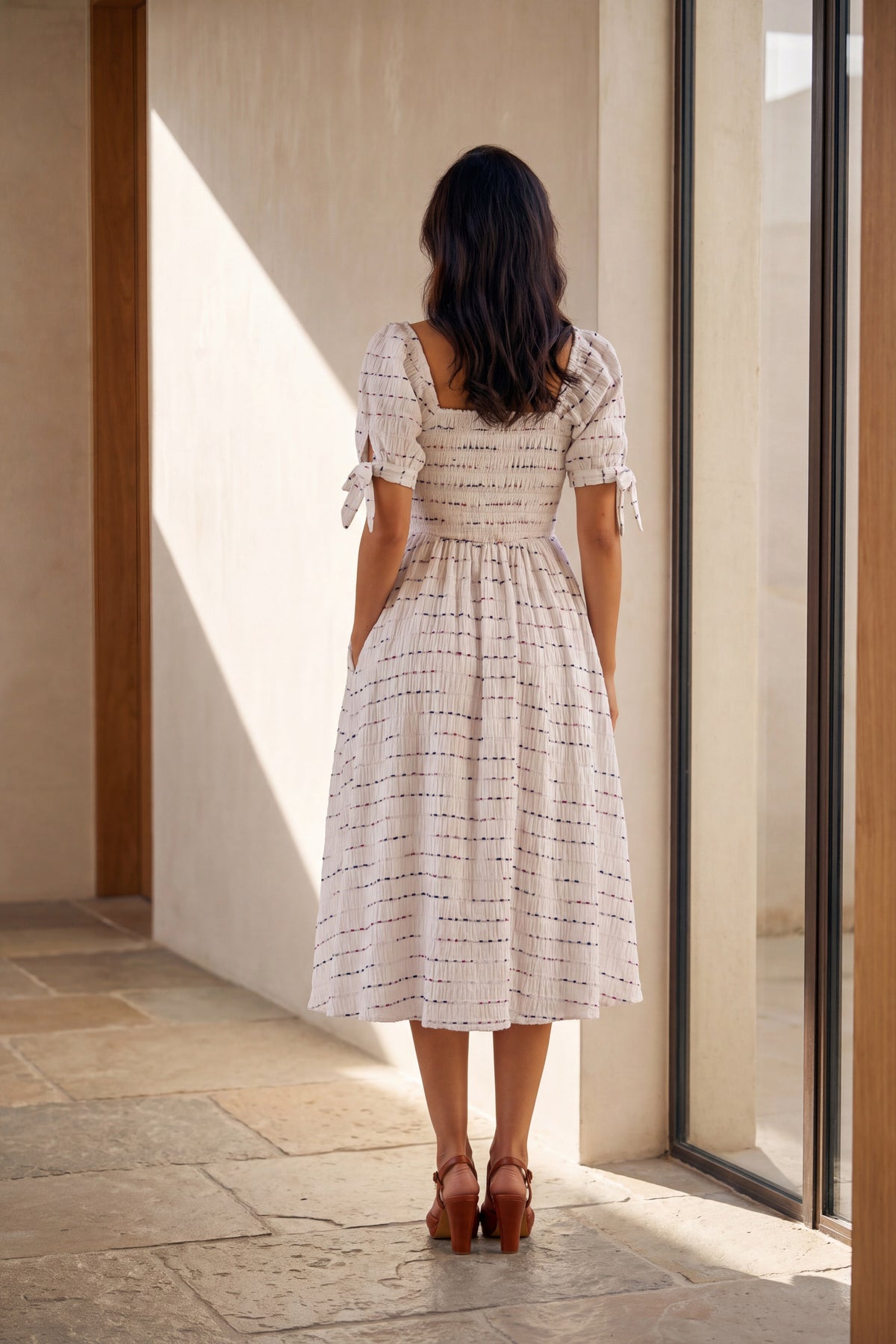 Rowan white smocked square neck midi dress, back view beside a tall window
