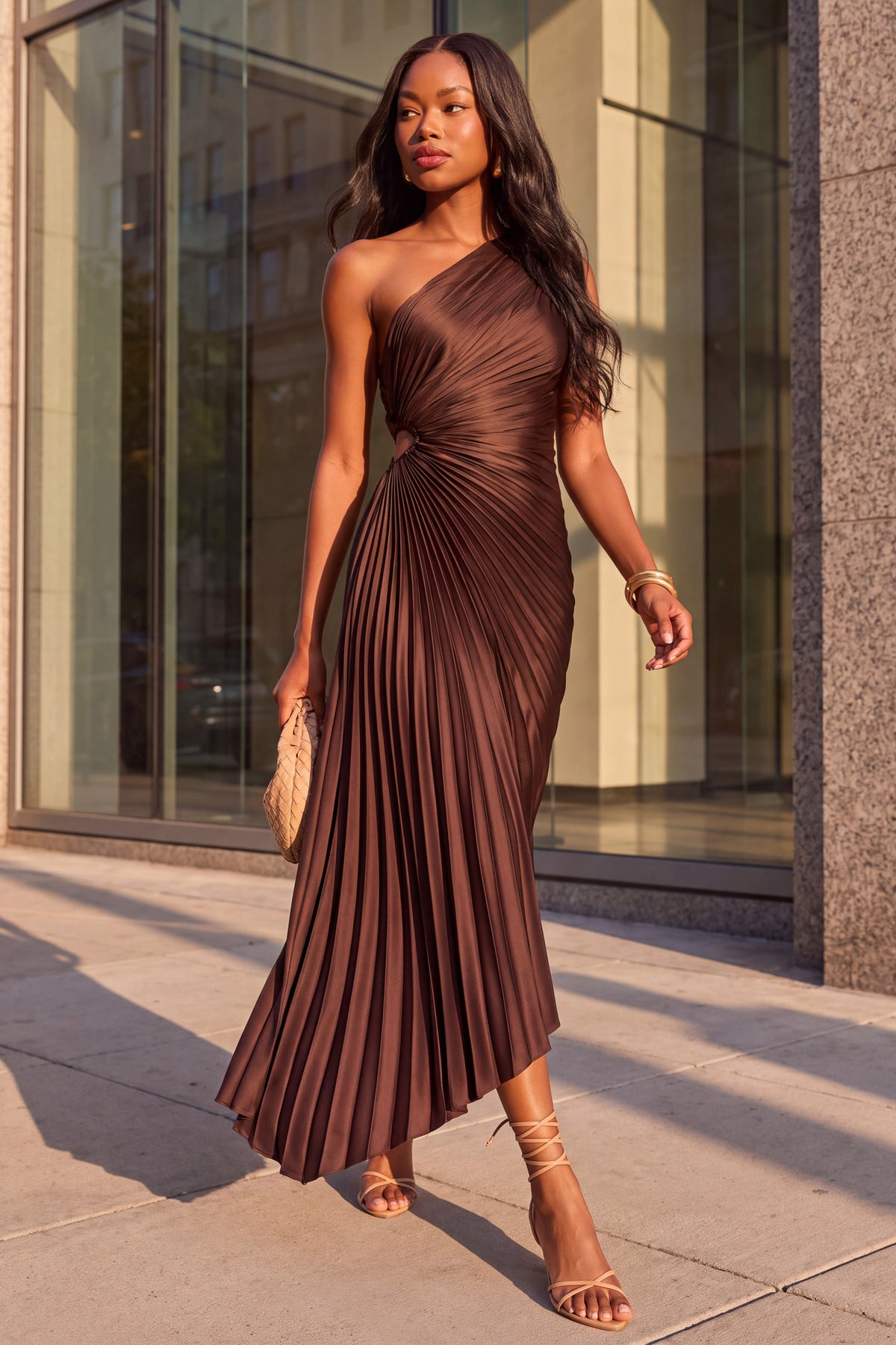 Solene chocolate pleated satin one shoulder maxi dress, worn walking past a glass fronted building