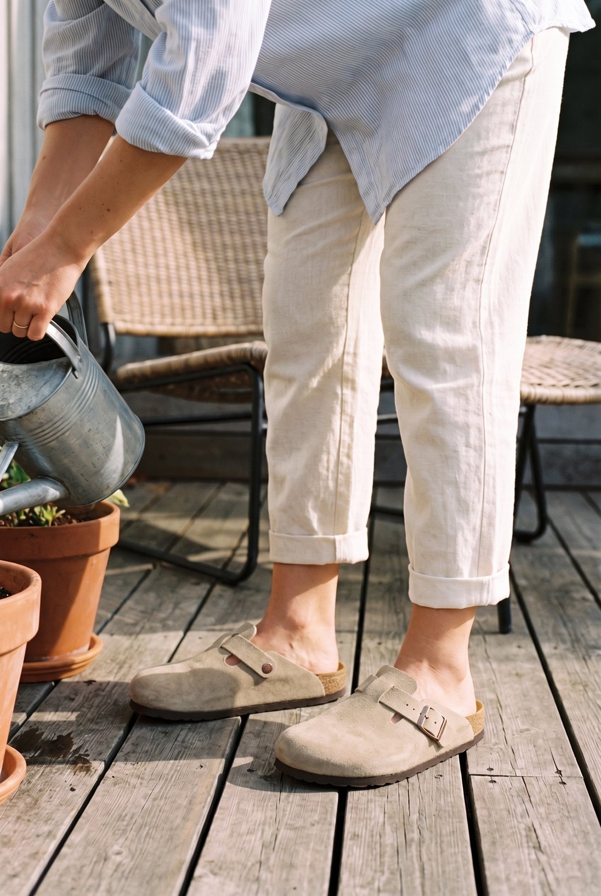 Marnie stone suede clogs worn with linen trousers while watering balcony plants.